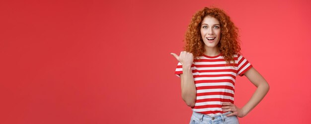 Foto sassy gutaussehende emotional glücklich lächelnde rothaarige europäische weibliche lockige frisur, die mit dem daumen nach links zeigt