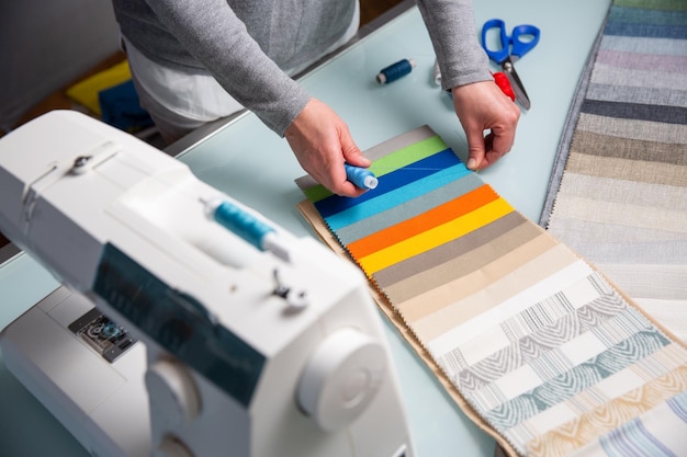 El sastre elige el color correcto de un hilo azul utilizando muestras de tela en la mesa durante el proceso de costura Concepto de artesanía de costura