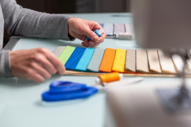 El sastre elige el color correcto de un hilo azul utilizando muestras de tela en la mesa durante el proceso de costura Concepto de artesanía de costura