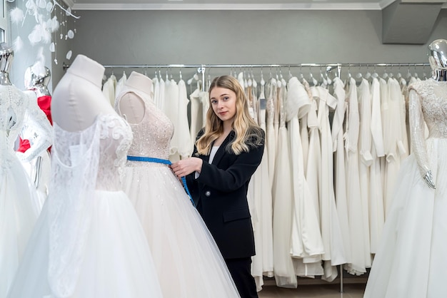 Sastre femenino midiendo elegante vestido de novia en maniquí usando cinta métrica