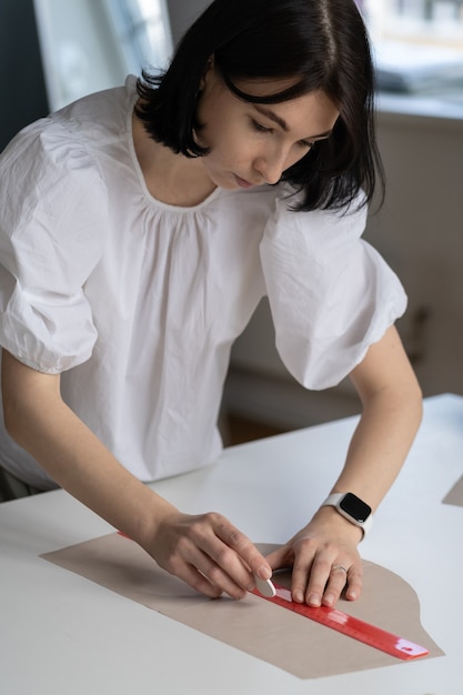 El sastre femenino usa una regla para dibujar la tela del patrón para cortar el diseñador de materiales o la costurera en el taller