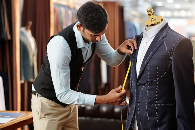 Foto sastre joven creativo midiendo chaqueta a medida en maniquí en el que está trabajando