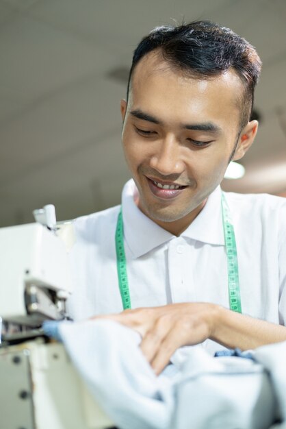 Sastre masculino asiático coser meticulosamente con una máquina de coser en una fábrica de ropa