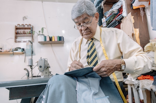 Sastre mexicano envejecido cosiendo a mano en negocios locales.