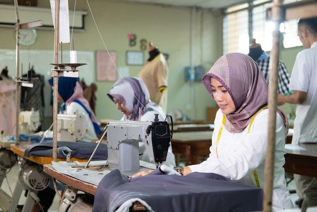 Sastre a mujer en hijab con una cinta métrica alrededor de su cuello usando una máquina de coser en el trabajo