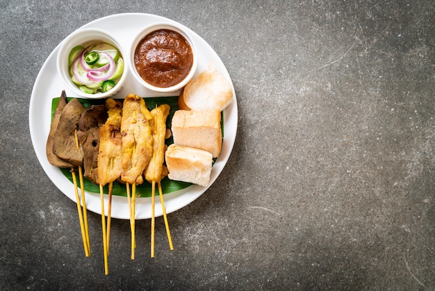 Satay de cerdo y satay de hígado con pan y salsa de maní y encurtidos que son rodajas de pepino y cebollas en vinagre - estilo de comida asiática