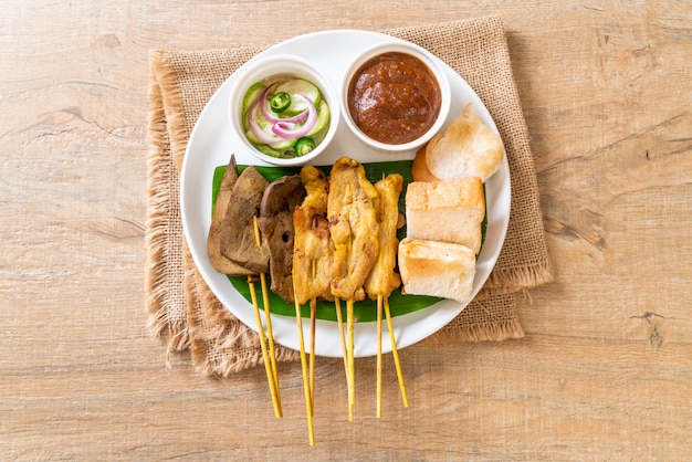 Satay de cerdo con su salsa de maní y encurtidos que son rodajas de pepino y cebolla en vinagre