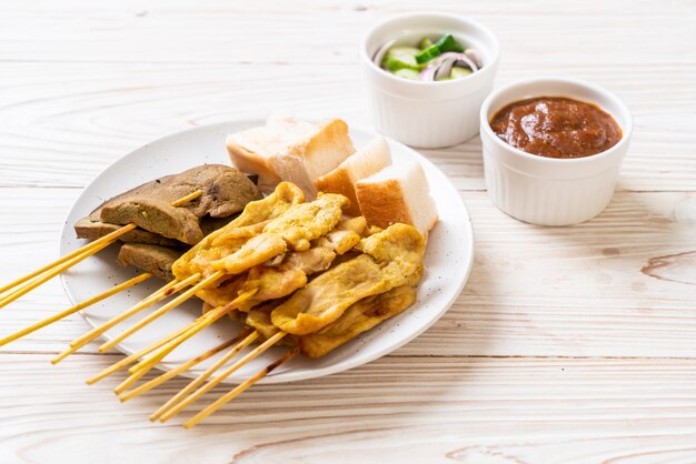 Satay de cerdo con su salsa de maní y encurtidos que son rodajas de pepino y cebolla en vinagre