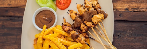 Satay de frango servido com molho de amendoim e batatas fritas. bali, estilo de vida banner, formato longo