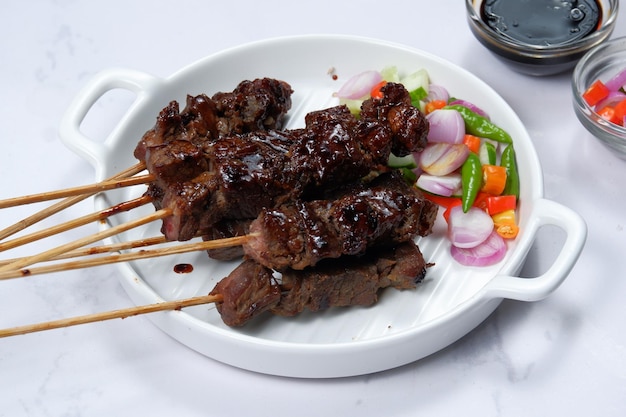 Satay oder Sate am Spieß und gegrilltes Fleisch, serviert mit würzigem Salat, Gurke, Chili und Sojasauce,