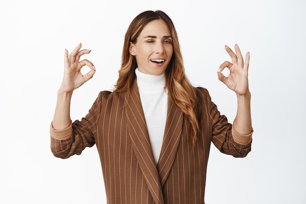 Foto satisfecha mujer corporativa de mediana edad asiente con la cabeza guiñando un ojo y sonriendo complacida mostrando ok bien gesto alabanza calidad recomendar empresa fondo blanco