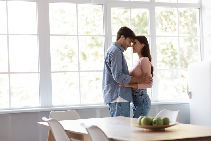 Foto satisfecho, alegre, joven esposo y esposa bailando y abrazándose juntos en el interior de la cocina