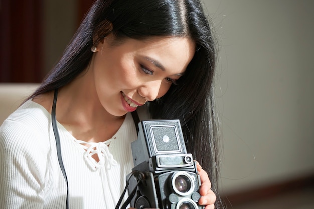 Satisfecho atractivo joven fotógrafo asiático con cabello negro mirando a través de fotos en cámara antigua