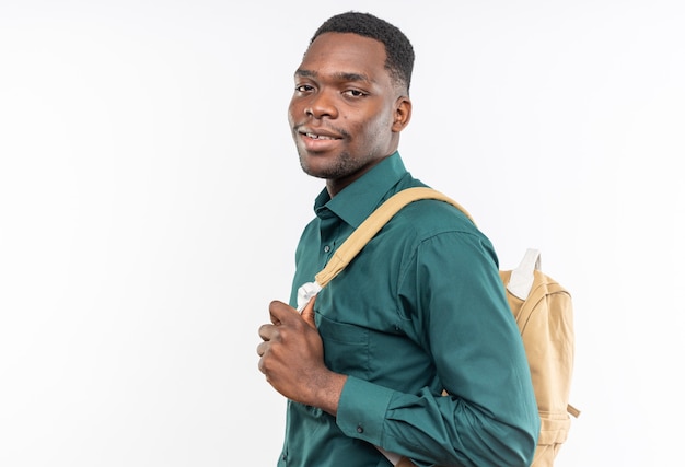 Satisfecho joven estudiante afroamericano con mochila de pie hacia los lados y mirando al lado