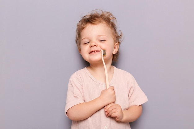 Satisfecho niño pequeño bebé sonriente disfrutando de cepillarse los dientes aislado sobre fondo gris sosteniendo cepillo de dientes sonriendo con cara encantada cuidado dental para niños