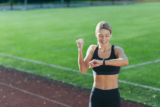 Satisfecho con el resultado de entrenar y correr el atleta mira el reloj inteligente la rubia