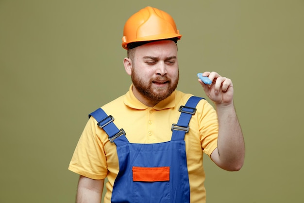 Satisfeito segurando marcador jovem construtor de uniforme isolado em fundo verde