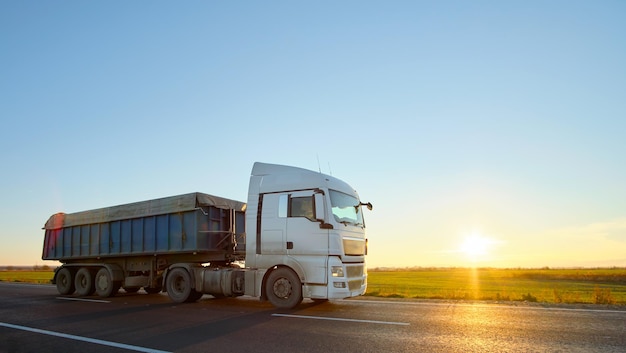 Sattelschlepper mit kippendem Frachtanhänger, der Sand vom Steinbruch transportiert, der auf der Autobahn am Abend Güter transportiert. Liefertransport- und Logistikkonzept.