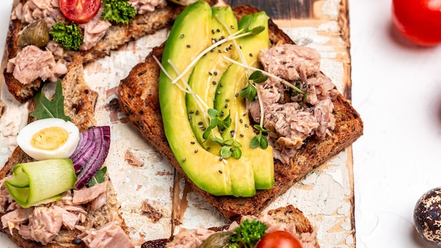 Satz Bruschettas mit Thunfisch Wachteleier Kirschtomaten Avocado Mikrogrün und Kapern auf hellem Hintergrund Toast mit Thunfisch leckere gesunde Lebensmittel Draufsicht