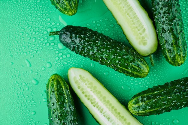 Satz frische ganze und geschnittene Gurken auf grünem Hintergrund mit Wassertropfen. Gartengurkentapete Hintergrunddesign