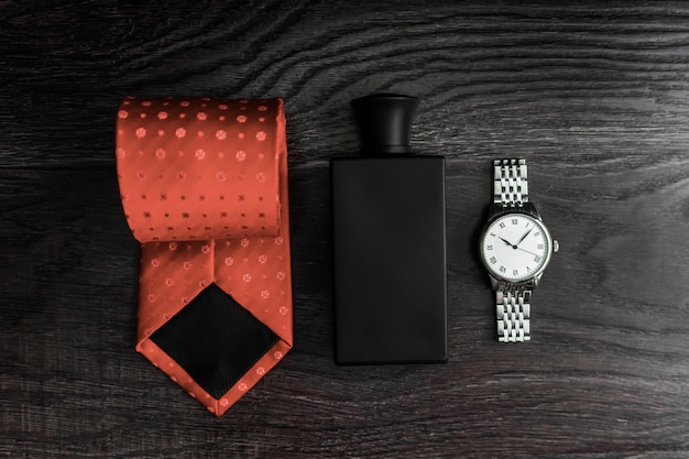 Satz Herrenaccessoires, Uhren, Krawatte, Parfums auf einem hölzernen dunklen Hintergrund.