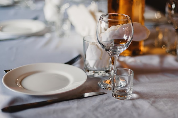 Satz leere Gläser und Teller mit Tischbesteck auf einer weißen Tischdecke auf dem Tisch im Restaurant