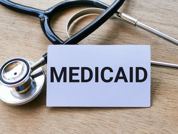 Satz MEDICAID auf weißer Karte mit Stethoskop geschrieben. Medizin- und Gesundheitskonzept.
