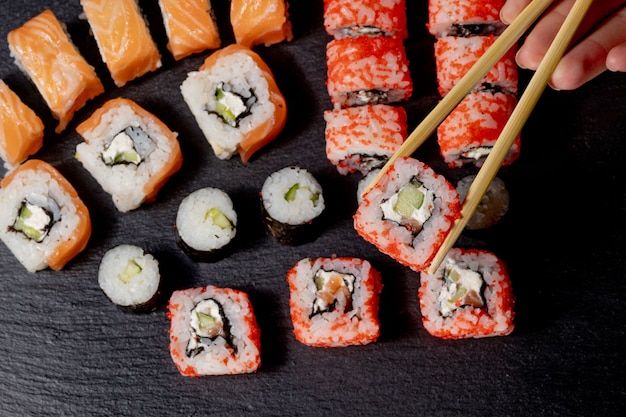 Satz Sushi-Rolle auf schwarzem Schiefer Hintergrundfutter Fisch Philadelphia Japanischer Lachs köstliche Sushi Reis Gurken Mahlzeit traditionelle Wasabi frische gesunde Gourmet rohe Küche.
