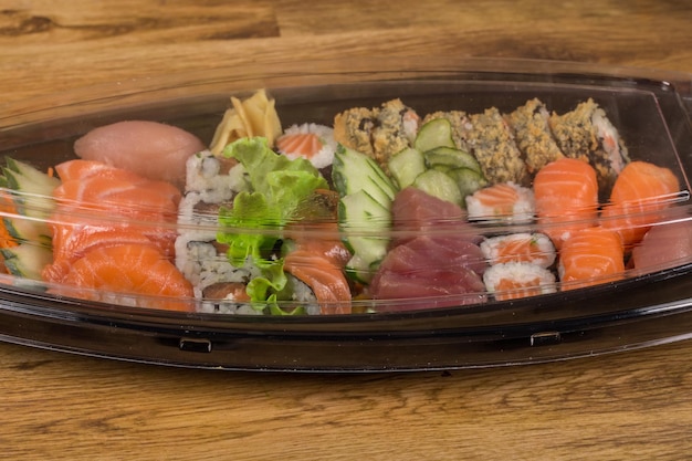 Satz Sushi-Rollen in Plastikbox auf Holztisch. Sushi zur Lieferung von Sushi in Kunststoffbox