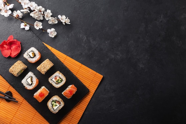 Satz Sushi- und Maki-Rollen mit Zweig weißer Blumen auf Steintisch. Ansicht von oben.