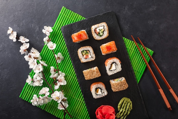 Satz Sushi- und Maki-Rollen mit Zweig weißer Blumen auf Steintisch. Ansicht von oben.