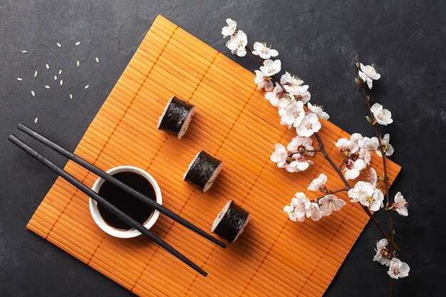 Satz Sushi- und Maki-Rollen mit Zweig weißer Blumen auf Steintisch. Ansicht von oben.