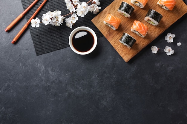 Satz Sushi- und Maki-Rollen mit Zweig weißer Blumen auf Steintisch. Ansicht von oben.