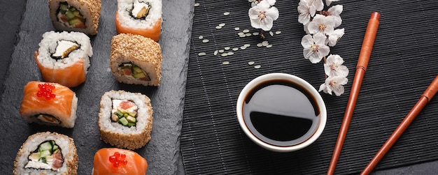 Satz Sushi- und Maki-Rollen mit Zweig weißer Blumen auf Steintisch. Ansicht von oben.