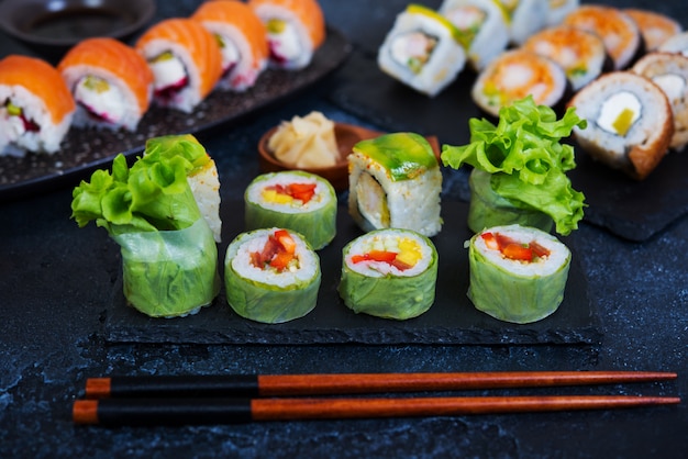 Satz vegetarische Sushi-Rollen mit Salatblättern, Gemüse und chinesischen Stäbchen auf einem schwarzen Hintergrund. Traditionelles japanisches Essen.