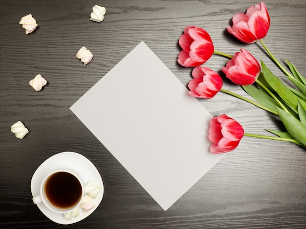 Sauberes blatt papier, rosa tulpen und eine tasse kaffee. schwarzer tisch. ansicht von oben