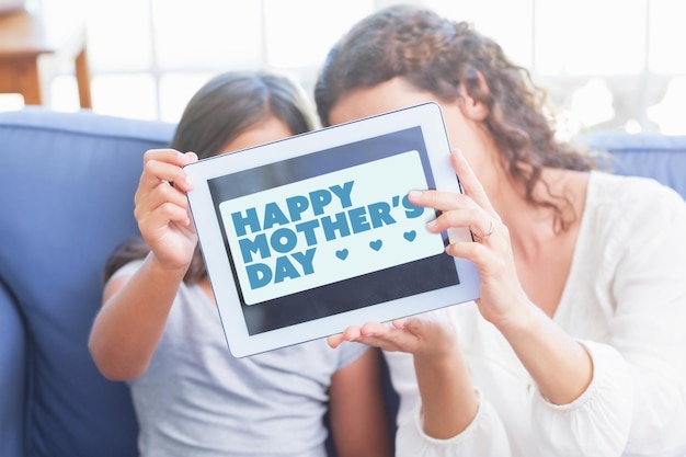 saudação do dia das mães contra feliz mãe e filha sentada no sofá e tomando selfie