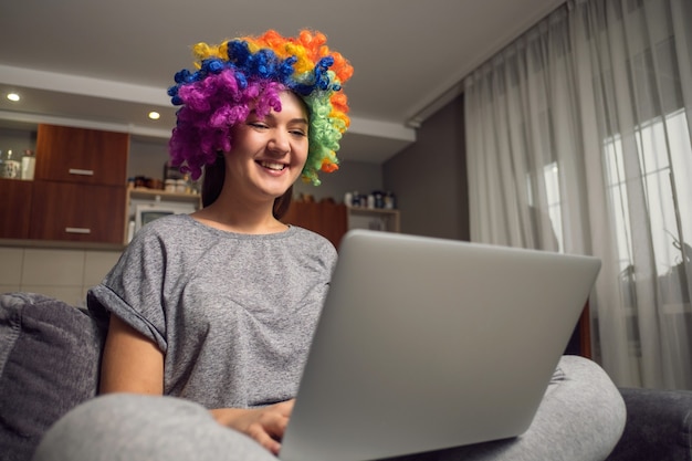 Foto saudações de feriado online, jovem se comunica em redes sociais com laptop, garota sentada em casa na cadeira com laptop, palhaço com laptop em casa, ri