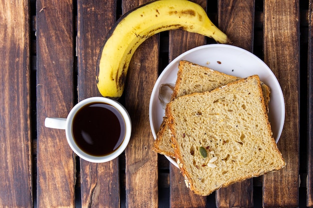 Saudável e saboroso café da manhã com café preto de pão multigrãos e banana em madeira