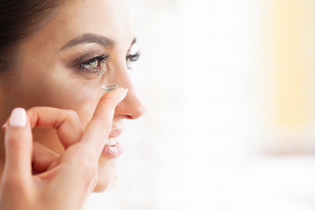 Saúde. A rapariga prende a lente de contato nas mãos. Retrato de uma mulher bonita com olhos verdes e lentes de contato. Olhar saudável. Alta resolução