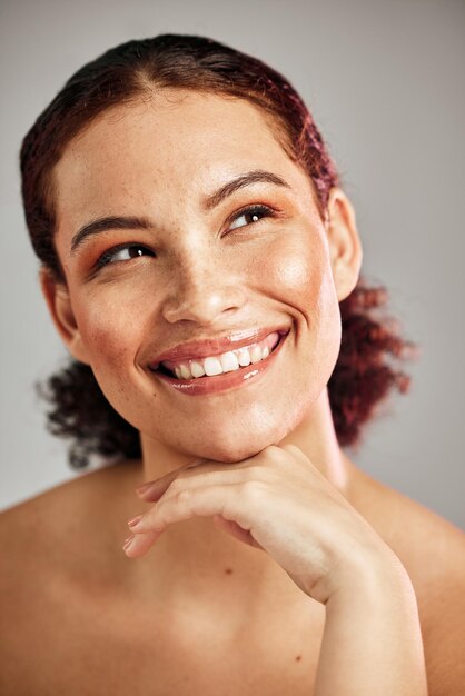 Foto saúde da pele e mulher com maquiagem em estúdio com uma beleza cosmética ou rotina de rosto natural sorriso feliz e modelo feminino com tratamento facial de bem-estar ou autocuidado isolado por fundo cinza