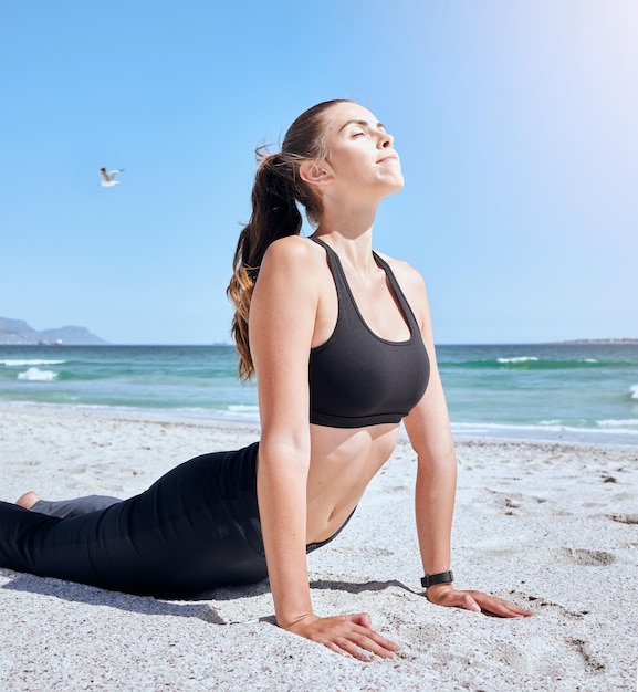 Saúde de ioga de praia e mulher alongando-se para treino de saúde corporal ou exercício de liberdade ao ar livre Pilates pose de cobra pose de paz no céu e treinamento de garotas para bem-estar mental na ilha tropical oceânica