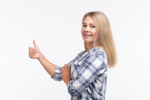 Saúde dos dentes, odontologia e correção de mordida - mulher sorridente feliz com aparelho aparecendo os polegares na parede branca.