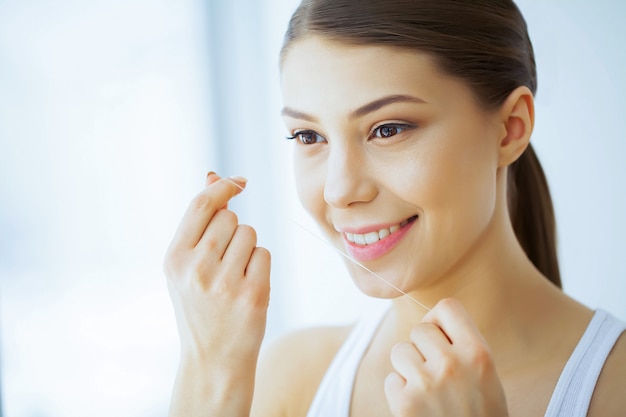 Saúde e beleza. A rapariga bonita com dentes brancos limpa os dentes com o fio dental. Uma Mulher Com Um Sorriso Bonito. Saúde dos Dentes