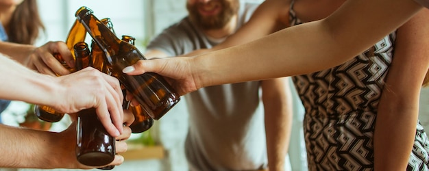 Saúde. Mãos de amigos, colegas durante o consumo de cerveja, se divertindo, tilintando garrafas, copos juntos.