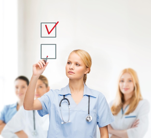 saúde, medicina e tecnologia - jovem médico ou enfermeiro com um marcador desenhando uma marca de seleção vermelha na caixa de seleção com a equipe no verso