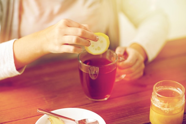 saúde, medicina tradicional e conceito de etnociência - close de mulher doente bebendo chá com limão, mel e gengibre em uma mesa de madeira