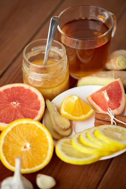 Foto saúde, medicina tradicional, remédio popular e conceito de etnociência - xícara de chá de gengibre com mel, frutas cítricas e alho em fundo de madeira