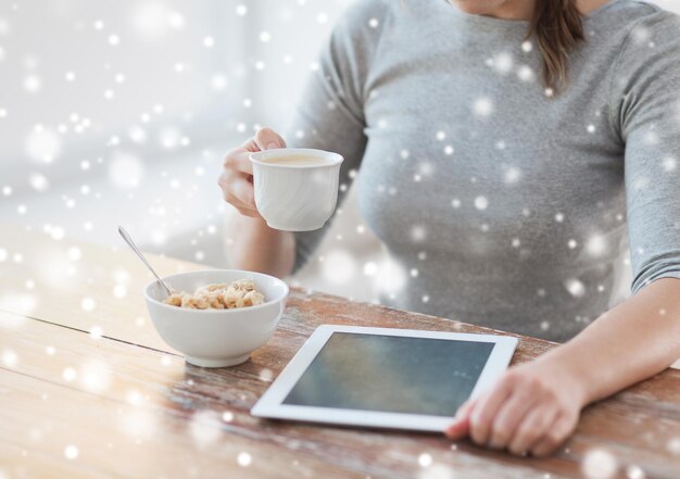 saúde, tecnologia, comida e conceito de casa - close-up de mulher com computador tablet pc tomando café da manhã e bebendo café