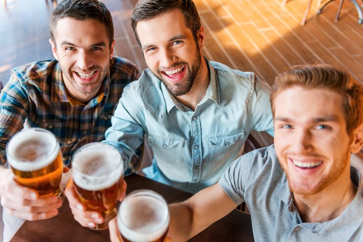 Foto saúde! vista superior de três jovens felizes em trajes casuais brindando com cerveja enquanto estão sentados em um bar